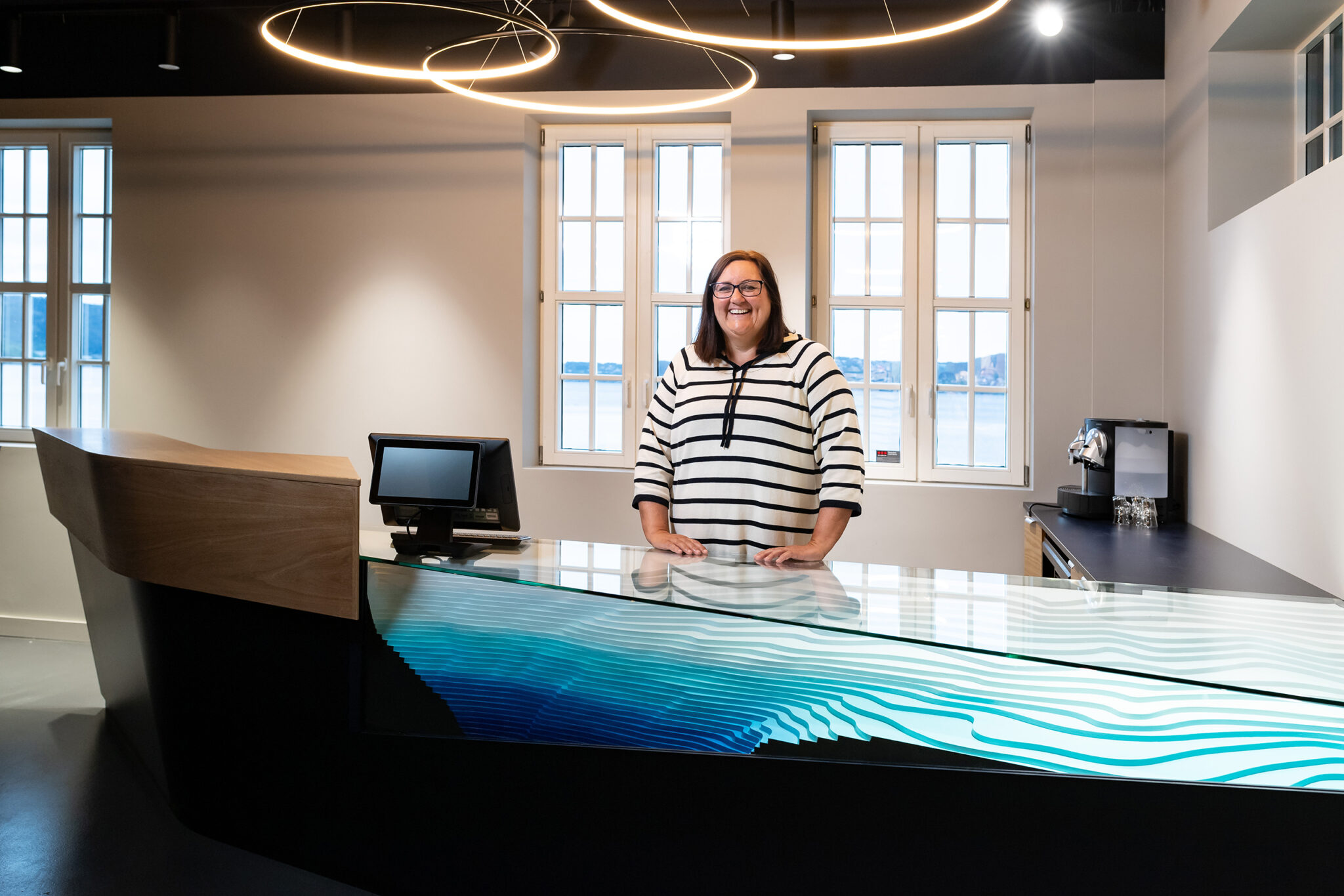 Resepsjonsdisk hos Store Blå med bølgemønster i glass og utsikt mot sjøen