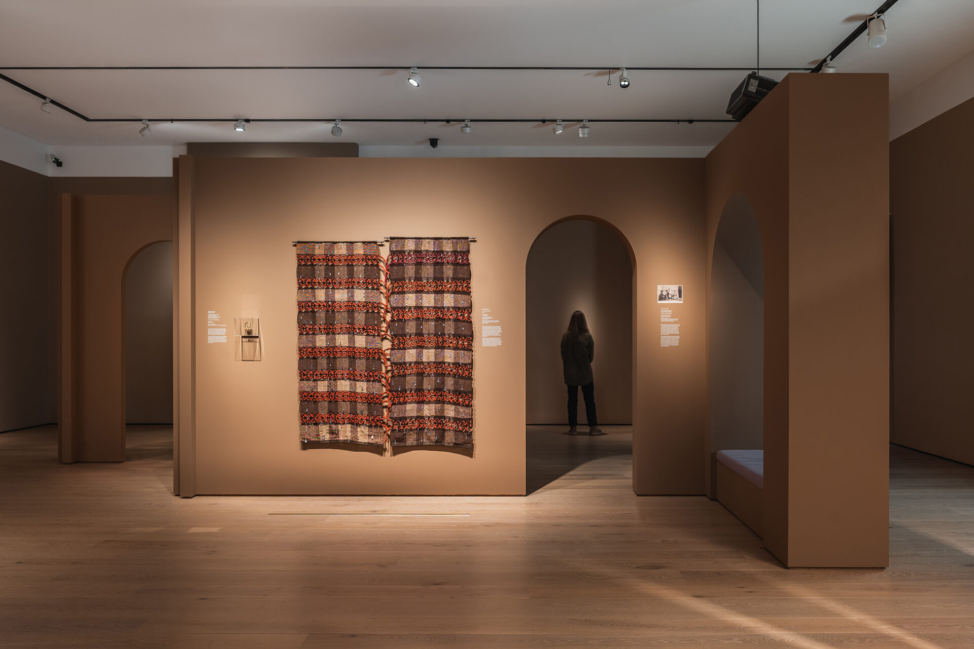 En person ser på et utstilt tekstil i en åpen del av utstillingen, som viser flyten i rommet.