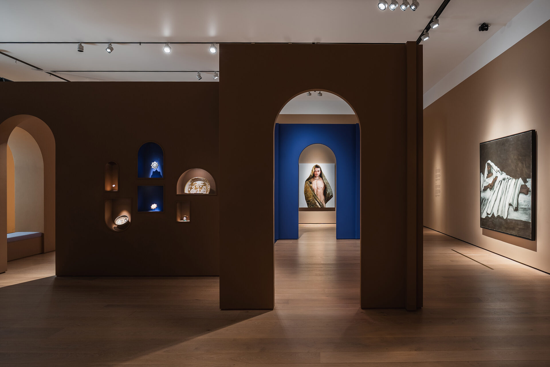 Oversikt over utstillingsvegg med integrerte nisjer for små objekter og en sentral buegang med dyp blå bakgrunn.