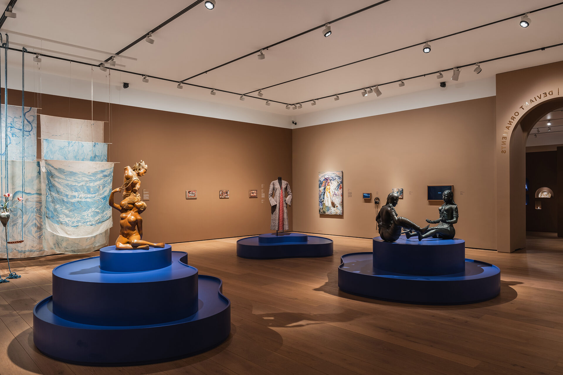 Vidvinkelbilde som viser romfølelsen i utstillingen med blå arkitektoniske elementer mot beige vegger og lys eikeparkett.