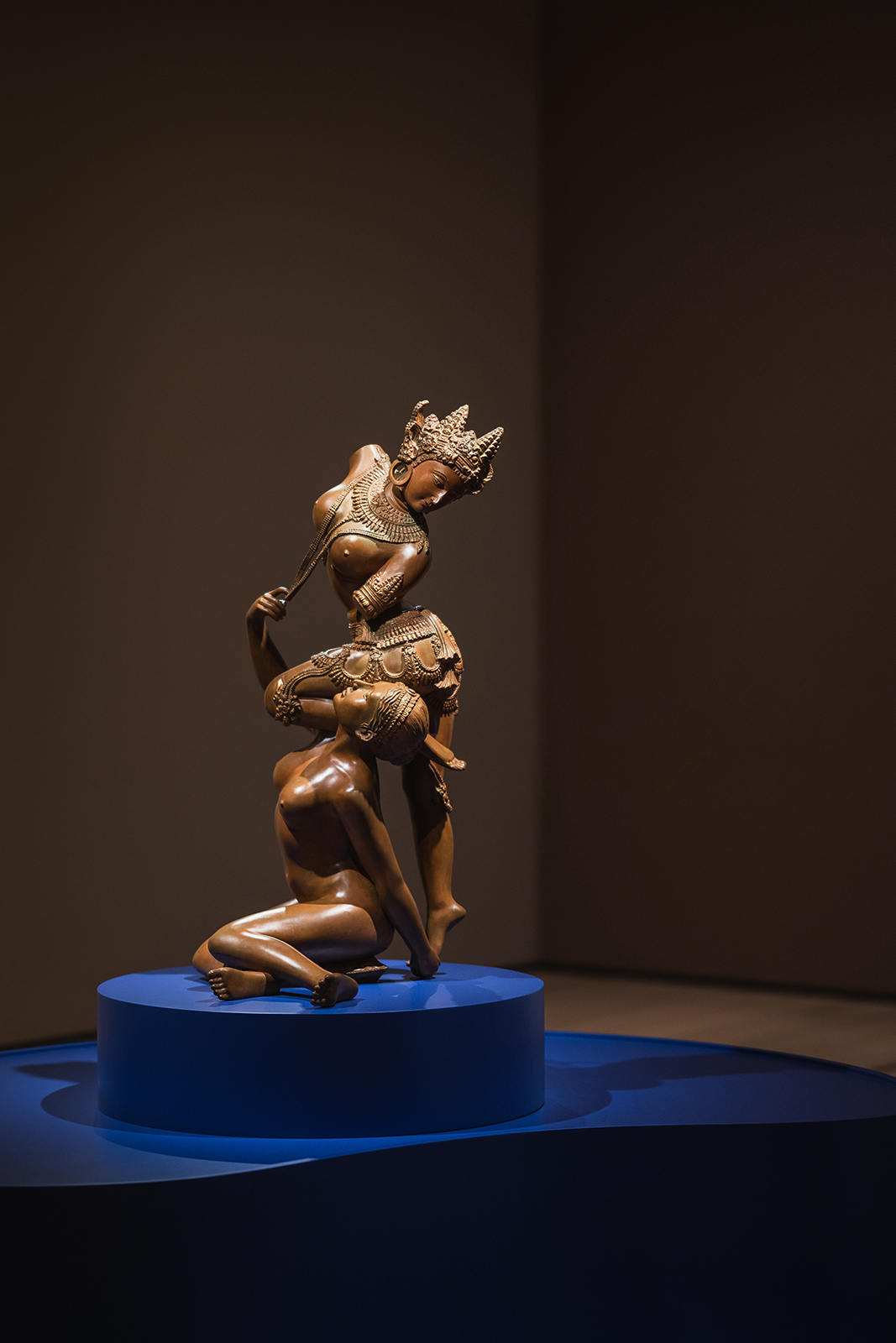 Detaljbilde av en brun skulptur av to figurer utstilt på en blå sokkel i utstillingen Deviant Ornaments på Nasjonalmuseet.