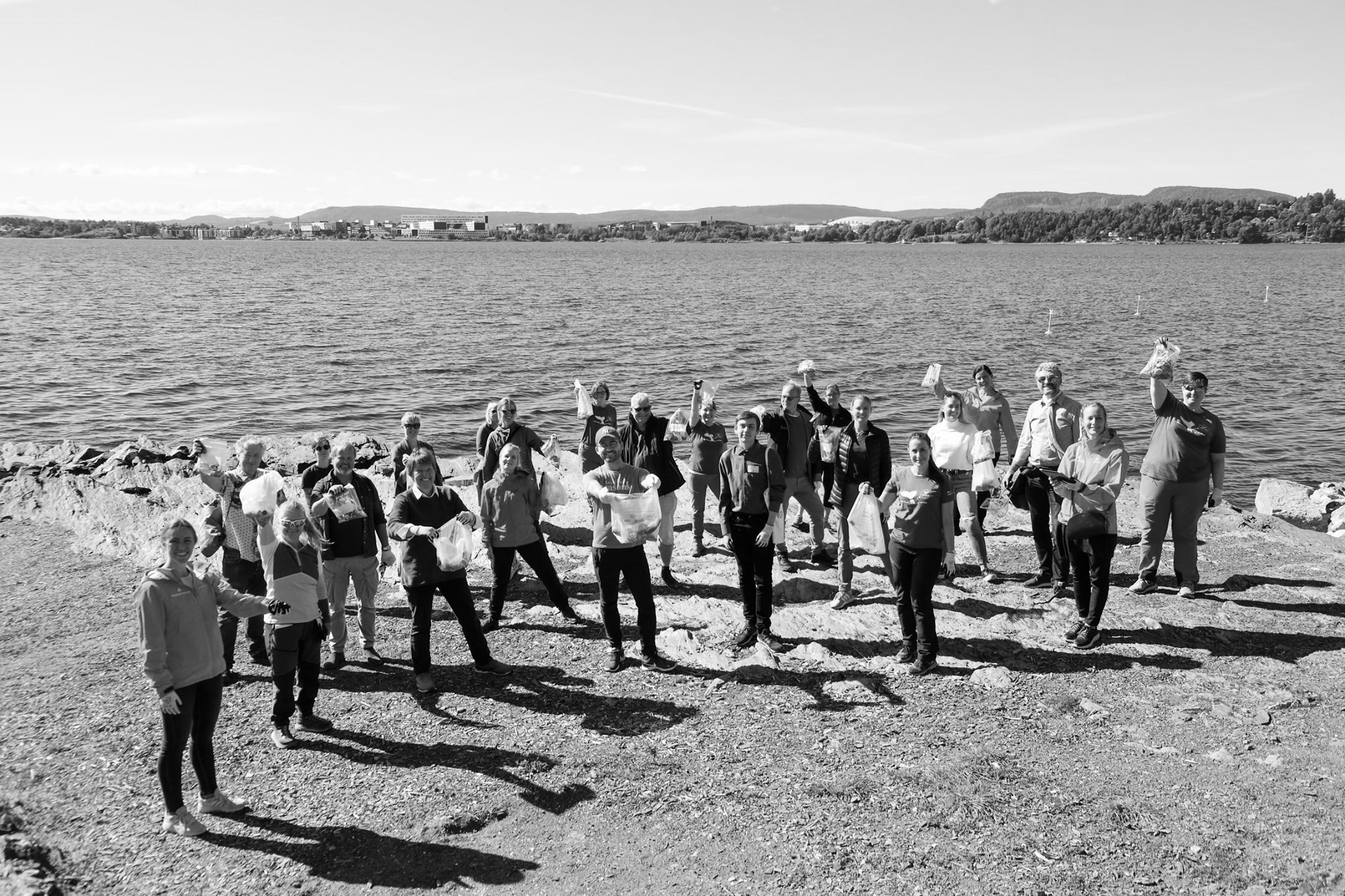 Ansatte og frivillige samlet på svaberget etter strandryddedugnad ved sjøen, med fylte søppelsekker.